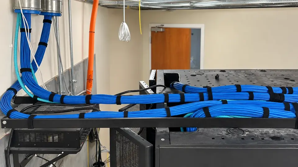 Illustrative supported blue network cable bundles entering equipment racks in a technical room.
