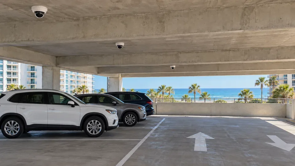 Coastal hotel parking garage with dome cameras mounted on the concrete ceiling above the drive lanes.
