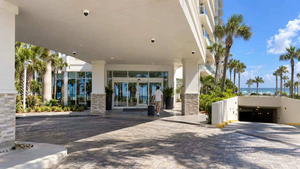 Coastal hotel arrival drive and garage entrance with white cameras mounted flush under the porte-cochere ceiling